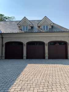 A stone home exterior featuring dark stained garage doors and dormer windows.