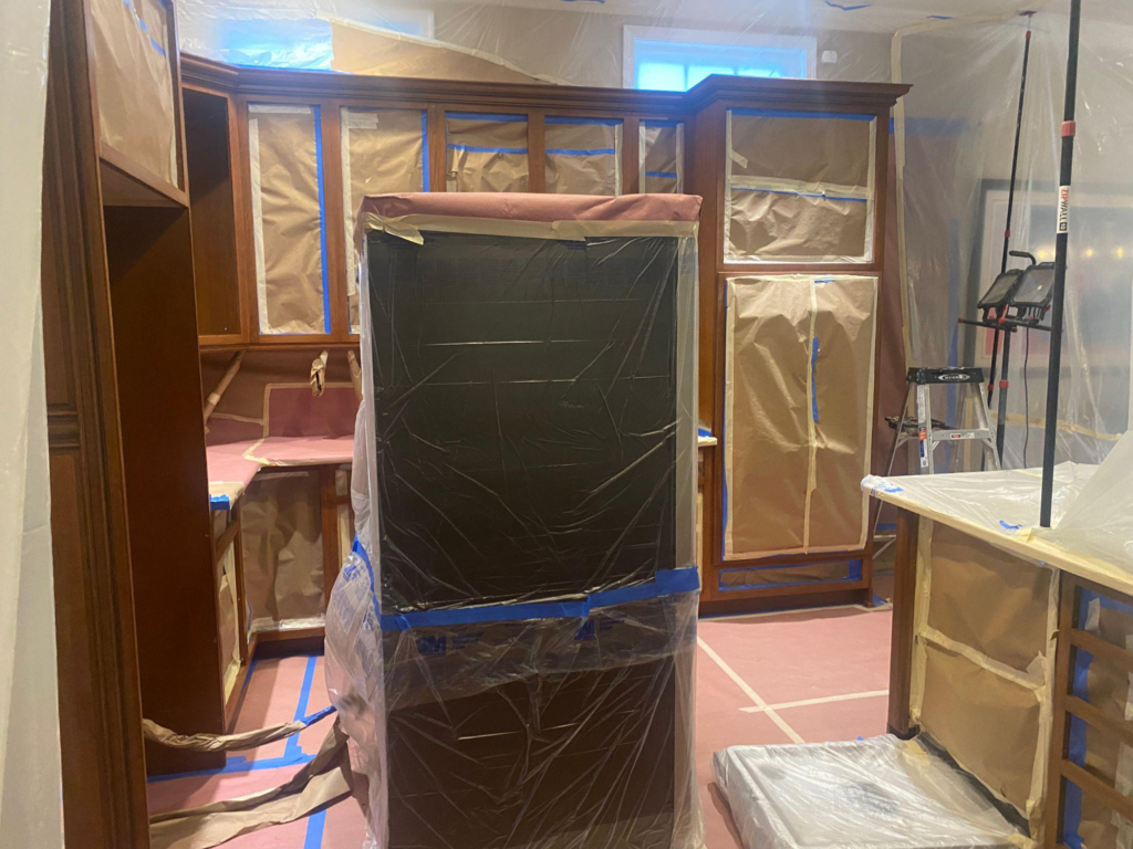 A kitchen with cabinets and appliances carefully taped and covered in preparation for a refinishing project.
