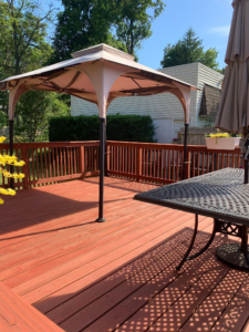 A stained wood deck with a canopy gazebo, patio table, and railing overlooking a backyard.