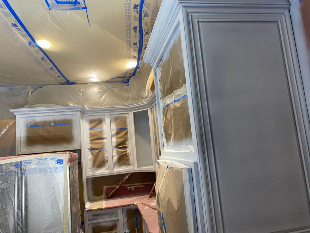 Freshly painted white kitchen cabinets with surrounding surfaces still taped and protected during a refinishing project.