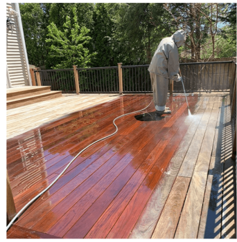 A worker in protective gear power washing a wood deck, revealing rich, restored wood beneath.